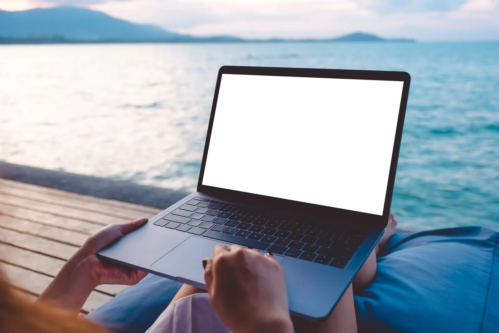 Open laptop with blank screen on a wooden pier overlooking the ocean at dusk