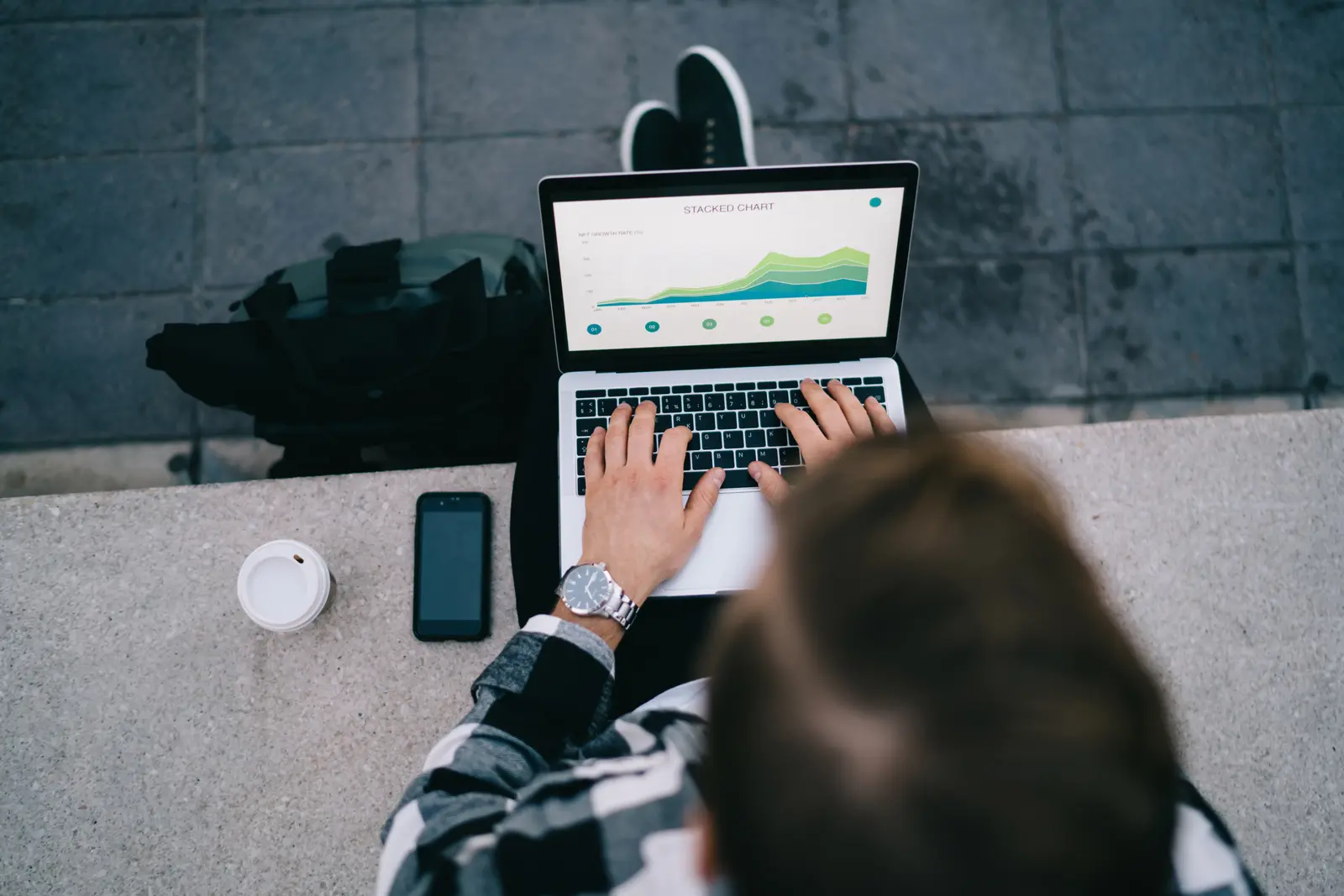 Person typing on a laptop showing a stacked-line growth chart, outdoor cafe setting